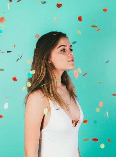 portrait of a beautiful girl in a white plunging neckline top looking to the right as it rains sparkling round confetti with a turquoise background