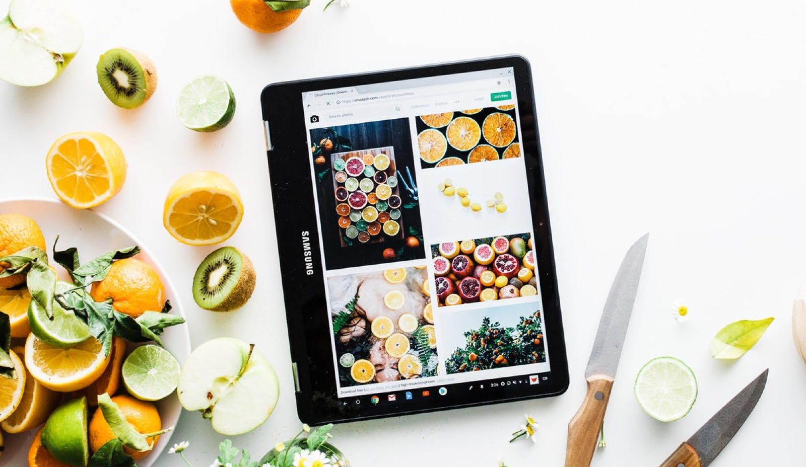 photo background: white surface filled with oranges and kiwis. photo foreground: ipad filled with different photos of oranges and grapefruits